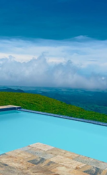 azurblauer Badepool - im Hintergrund schweben weiße Wolken am blauen Himmel über der tiefer gelegenen grünen Landschaft