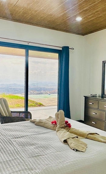 Doppelbett im Schlafzimmer 1 mit Blick durch die bodentiefen Fenster in die offene Landschaft