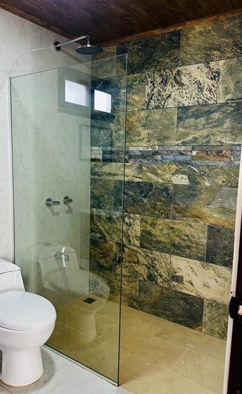 Gefließtes Bad mit Toilette und Dusche, abgetrennt durch eine Glasscheibe