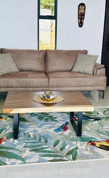 Sofa und Tisch stehen auf einem bunten Papageien-Teppich mit Blättern